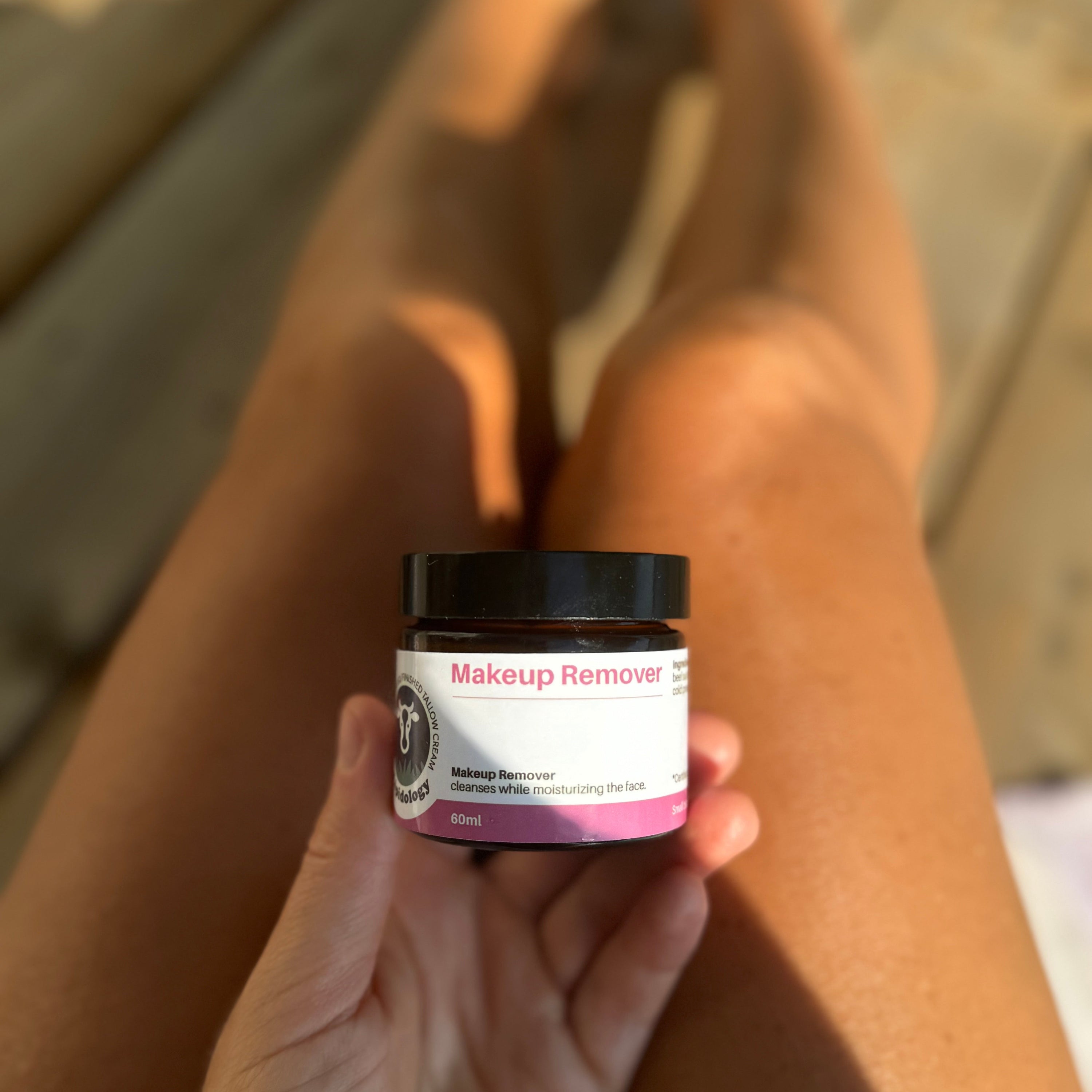 Hand holding a jar of makeup remover with a blurred background